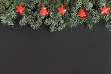 Christmas border with fir branches and red Christmas decorations on black background.