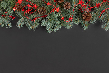 Christmas border with fir branches, cones and a red garland on a black background.