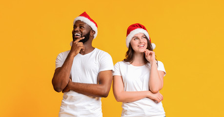 Obraz premium Pensive couple wearing santa hats and posing with thoughtful face expression