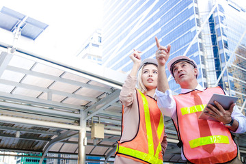 Western male and female engineers wear white safety hats and carry tablets. Standing for meetings outside the building Point your finger to the top to check the job. with copy space.