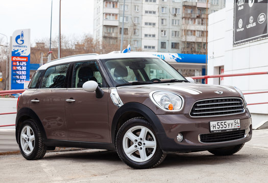  An expensive car, a female model of a mini cooper countryman beige and gold color and a white roof polished and shiny is set up in a street parking