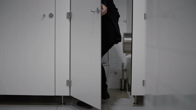 Businessman running into toilet cabin.