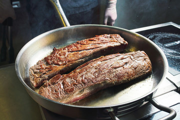 The chef works in the kitchen of the restaurant. Fresh meat roasted in a large frying pan. Restaurant kitchen background