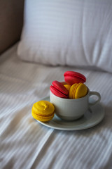 Colorful French macaron pastries in a white circle on the white linen in bed. Red and yellow pasta.