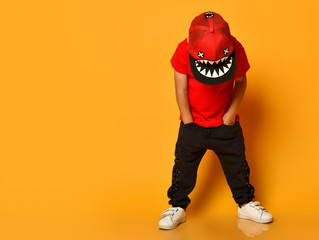 Young guy boy in a red T-shirt and dark pants, white sneakers and a funny cap posing on a free copy...