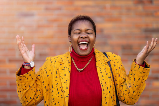 Joyous Woman With Arms Raised In Front Of A Wall 