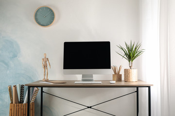 Workplace with computer and plant on wooden table. Light blue and white background