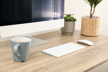 Workplace with computer, cup of coffee and plants on wooden table, close up