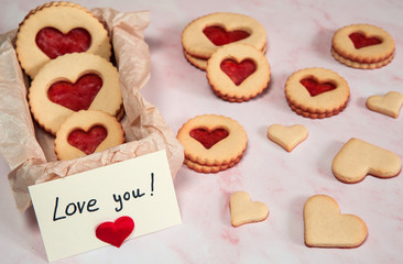 The Concept Of Valentine's Day. Homemade cakes for the holiday. A box of cookies in the shape of hearts, a note with a Declaration of love on a pink marble background. Selective focus.