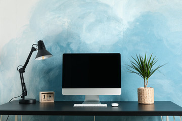 Workplace with computer and plant on wooden table. Blue and white background