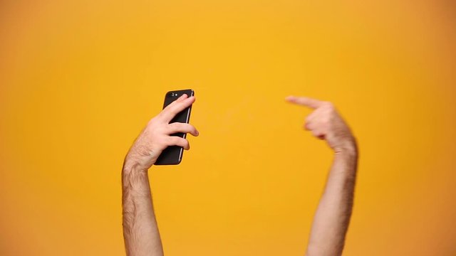 Man hold in hand mobile phone, using cellphone, showing fist win thumbs up isolated on yellow background in studio. Copy space for advertisement. With place for text or image. Advertising area mock up