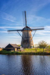 Famous Kinderdijk village of mills, popular tourist attraction in Netherlands (Holland), outdoor travel vertical background. Scenic landscape with windmill, water, green grass and blue sky with clouds