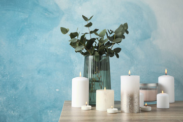 Burning candles and vase with eucalyptus against blue background, space for text