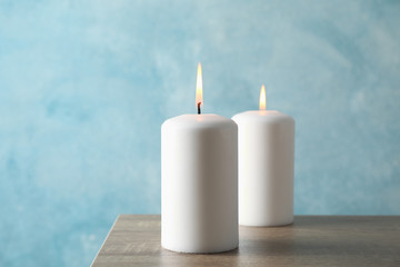 Fototapeta na wymiar Two burning candles on grey table against blue background, close up