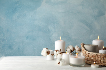 Burning candles, basket and cotton on white wooden table, space for text