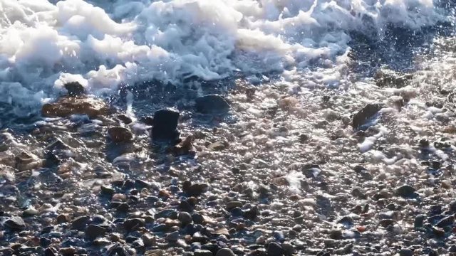 Slow motion sea waves with white foam washing up pebble stones on the beach