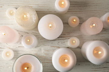 Different burning candles on wooden background, top view