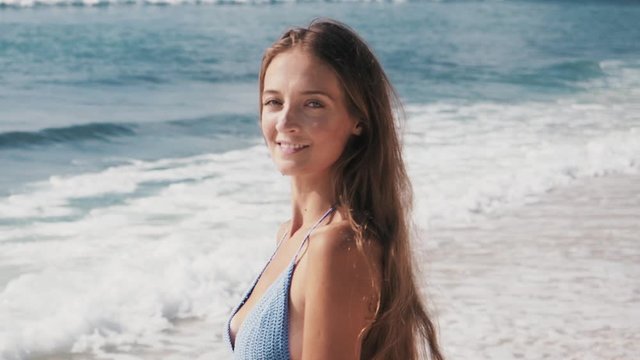 Woman in a blue swimsuit smiles and straightens her hair on a tropical beach