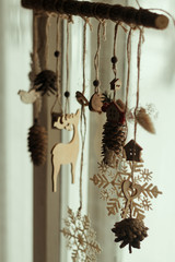  Wooden Christmas decor on a pine branch made of cones, snowflakes, dried flowers, toys (wooden deer, bird, key, house) weighs on a window background