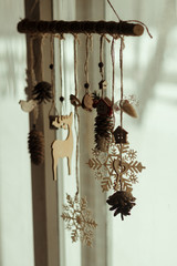  Wooden Christmas decor on a pine branch made of cones, snowflakes, dried flowers, toys (wooden deer, bird, key, house) weighs on a window background