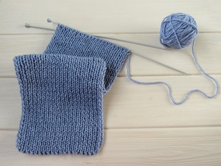 A blue wool scarf, knitting needles and a ball of yarn on a white table. There is room for text. Flat lay.