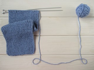 Blue scarf and ball of yarn on white background. The handmade scarf is knitted on spokes. There is room for text. Flat lay.