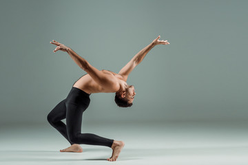 side view of handsome dancer with closed eyes in black leggings dancing contemporary on dark...