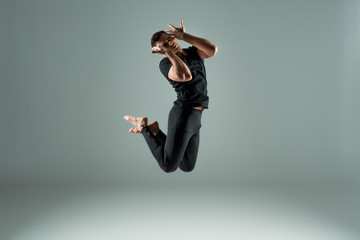 handsome dancer with closed eyes in black leggings and t-shirt dancing contemporary on dark...