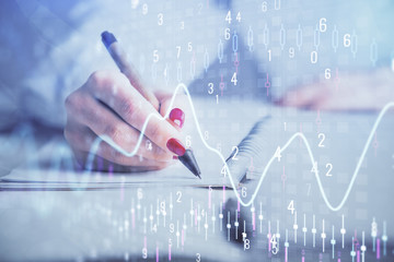 Double exposure of woman's hands making notes with forex graph hologram. Concept stock market analysis.