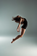 side view of dancer in black bodysuit dancing contemporary on grey background