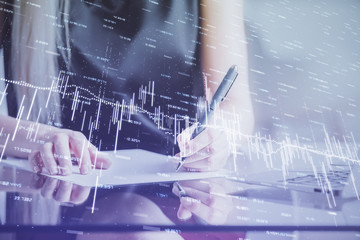 Naklejka premium A woman hands writing information about stock market in notepad. Forex chart holograms in front. Concept of research.