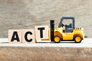 Toy forklift hold letter block t to complete word act on wood background