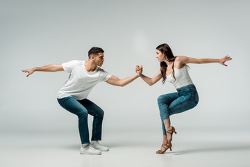 side view of dancers in denim jeans dancing bachata on grey background