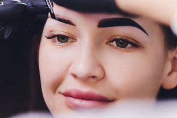 beautician- makeup artist applies paint henna on previously plucked, design, trimmed eyebrows in a...
