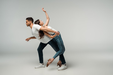 side view of dancers in denim jeans dancing bachata on grey background