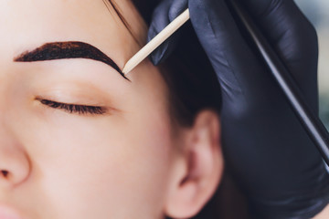 beautician- makeup artist applies paint henna on previously plucked, design, trimmed eyebrows in a...
