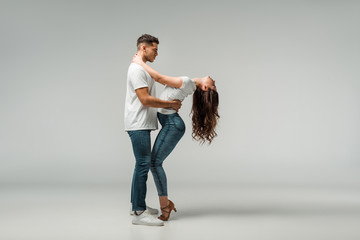 side view of dancers in t-shirts and jeans dancing bachata on grey background