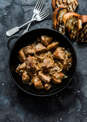 Roast pork with onion, garlic and hot pepper in a cast iron pan on a dark background, top view