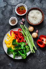 Ingredients for vegetarian paella - fresh vegetables sweet peppers, broccoli, asparagus, rice and spices on dark background, top view