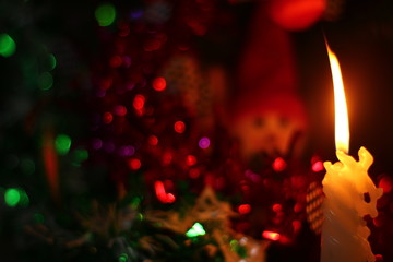 Light candles on the background of a Christmas tree with decorative lights.