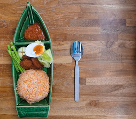 Traditional Thai food, spicy rice with herbs, egg and fried chicken with hot sauce, in a dish in the form of a boat