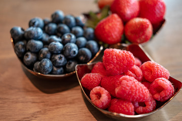 Fresh raspberries , blueberries, strawberry in the copper bowls on rustic natural wooden background