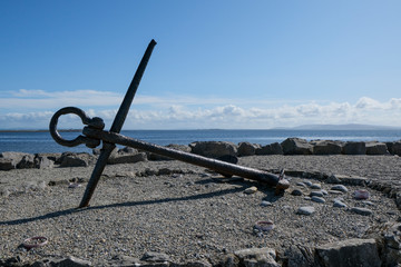 Large anchor on Salthill promenade with Galway bay and rain clouds in the background. Taken in Ireland in summer.