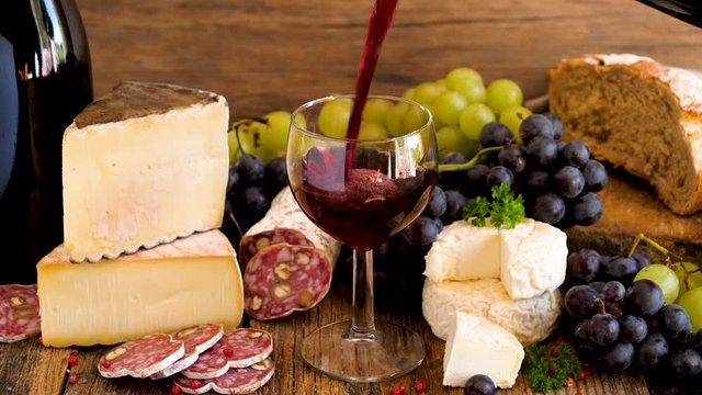 red wine pouring in a glass with bread, cheese, grape and salami composition