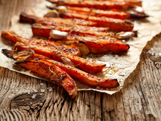 Sweet potato fries, baked fries with herbs and spices  on a  paper on a wooden rustic table, close up. Healthy vegetarian food