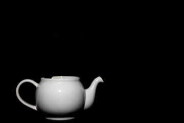 Photo of a white ceramic kettle with shadows from light and a black background.