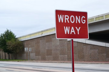 Wrong Way sign by freeway overpass city roads, safety law danger driving road rules concept.