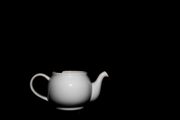 Photo of a white ceramic kettle with shadows from light and a black background.