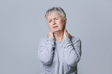 Senior woman suffering from neck pain on grey background