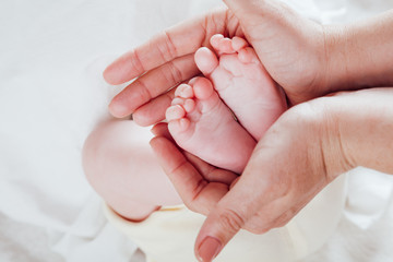 mom's hands hold the feet toes baby